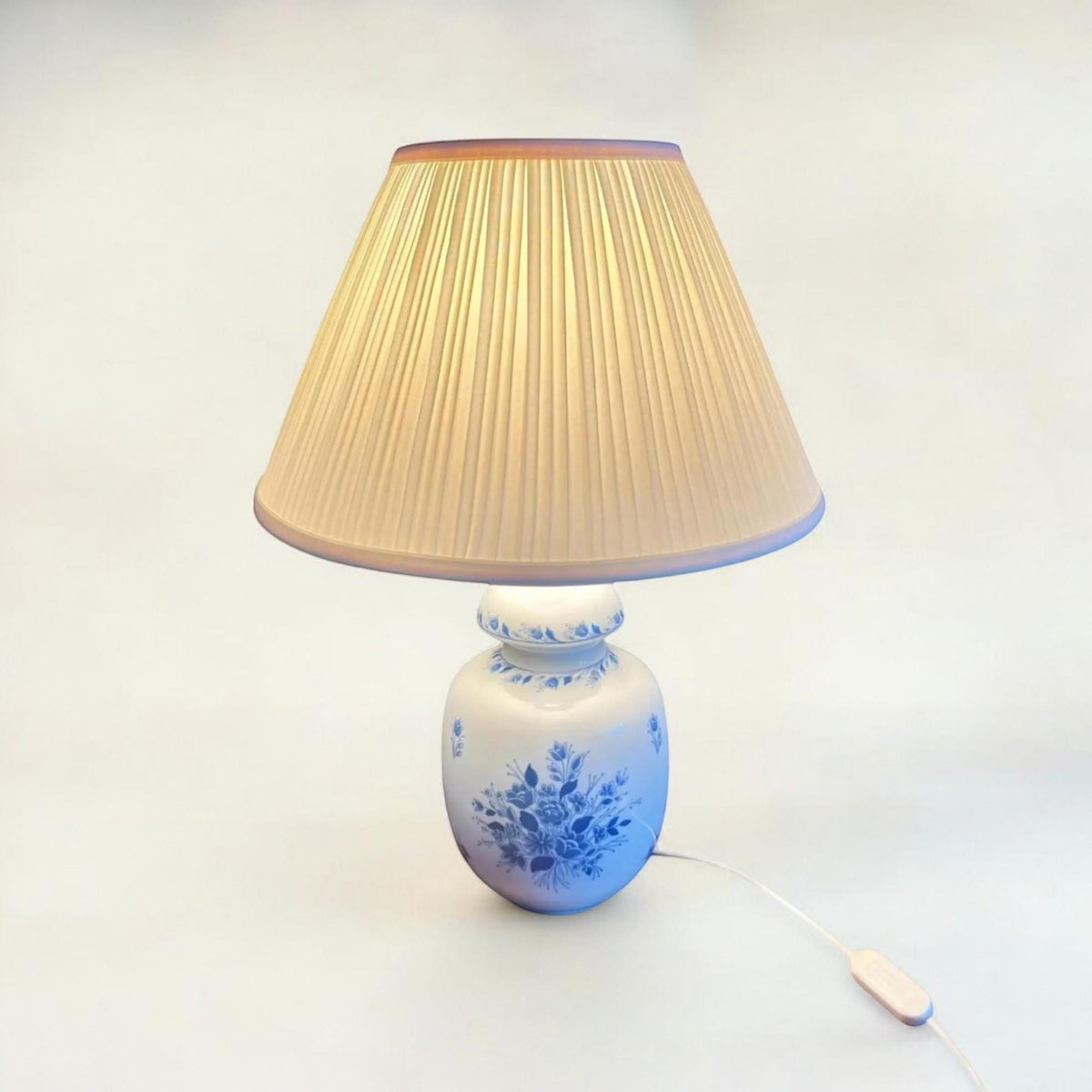Griechische Mid Century Pegasos Hellas Porzellan Tischlampe mit Plissee-Schirm. Der Porzellanfuß zeigt ein graziles blaues Blumendekor.